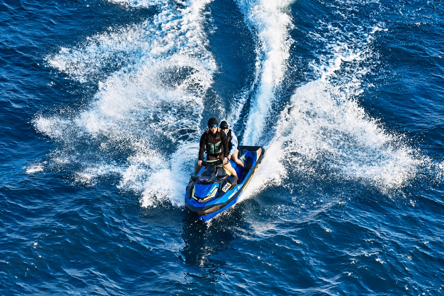 A rider steers a personal watercraft across dark water, leaving a broad white wake.