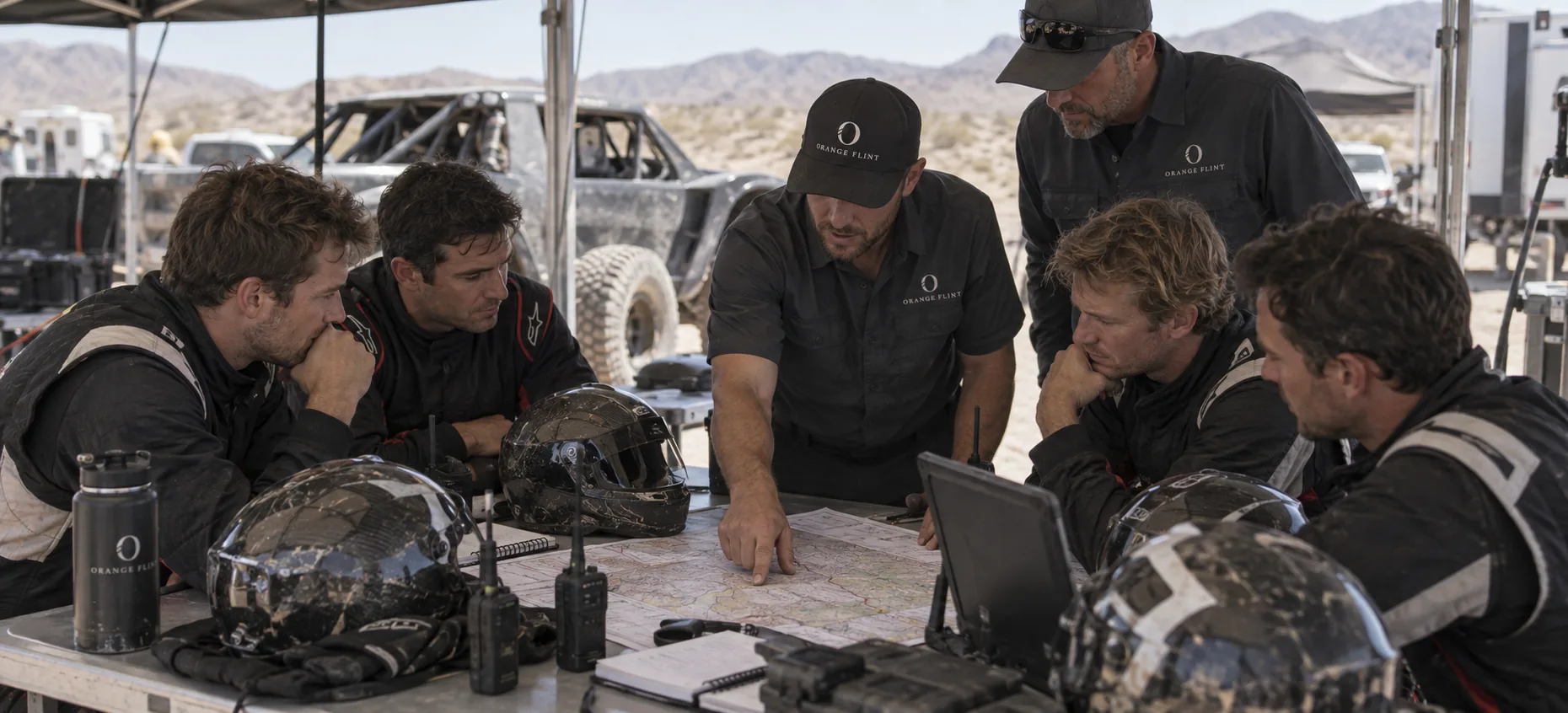 Four drivers in racing suits study a course map with Orange Flint staff.