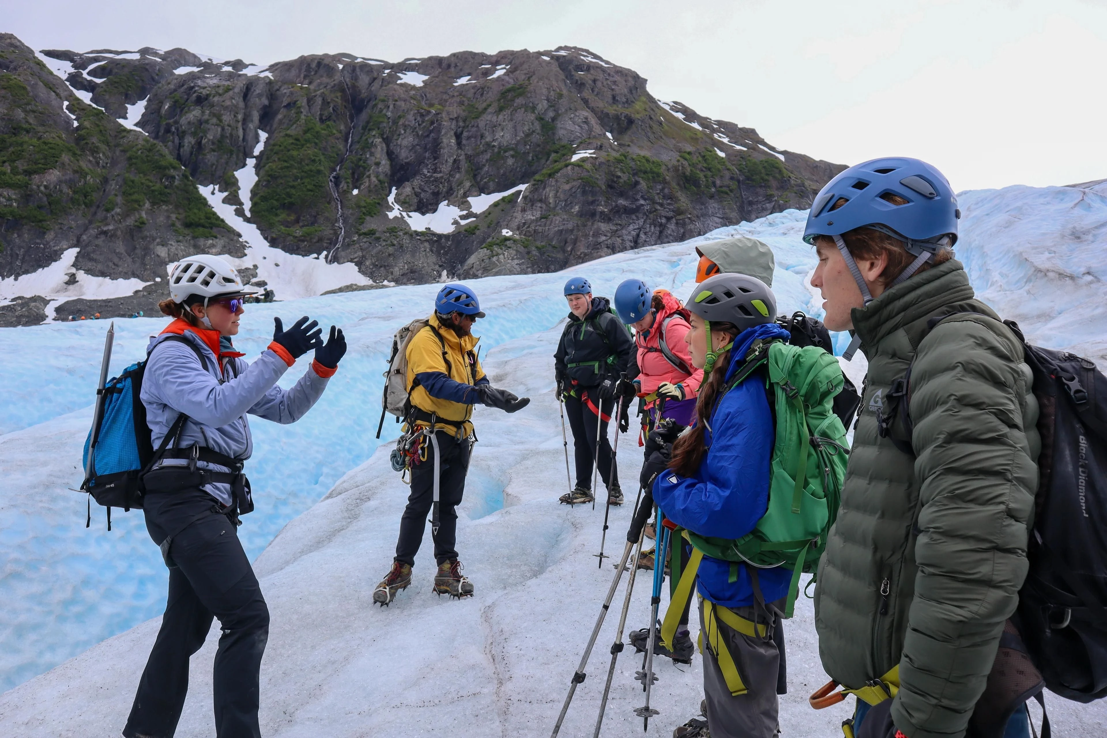 A helmeted group listens to a glacier guide, equipped with crampons, ropes and ice axes.