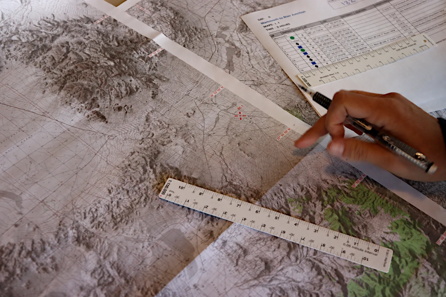 A navigator works with a pencil, paper topographic map and measuring rulers.