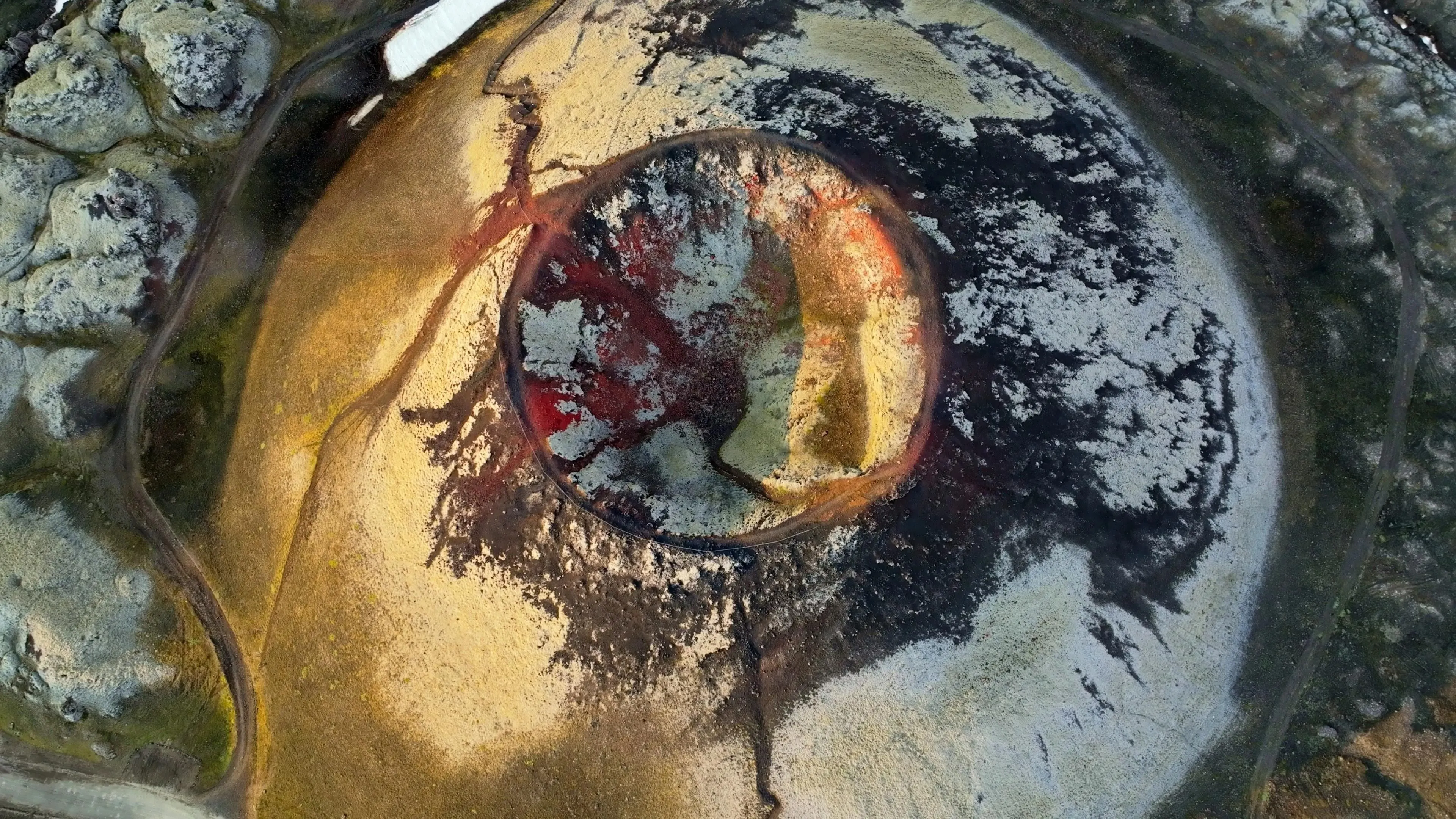 Aerial view of a colourful volcanic crater and surrounding lava fields.