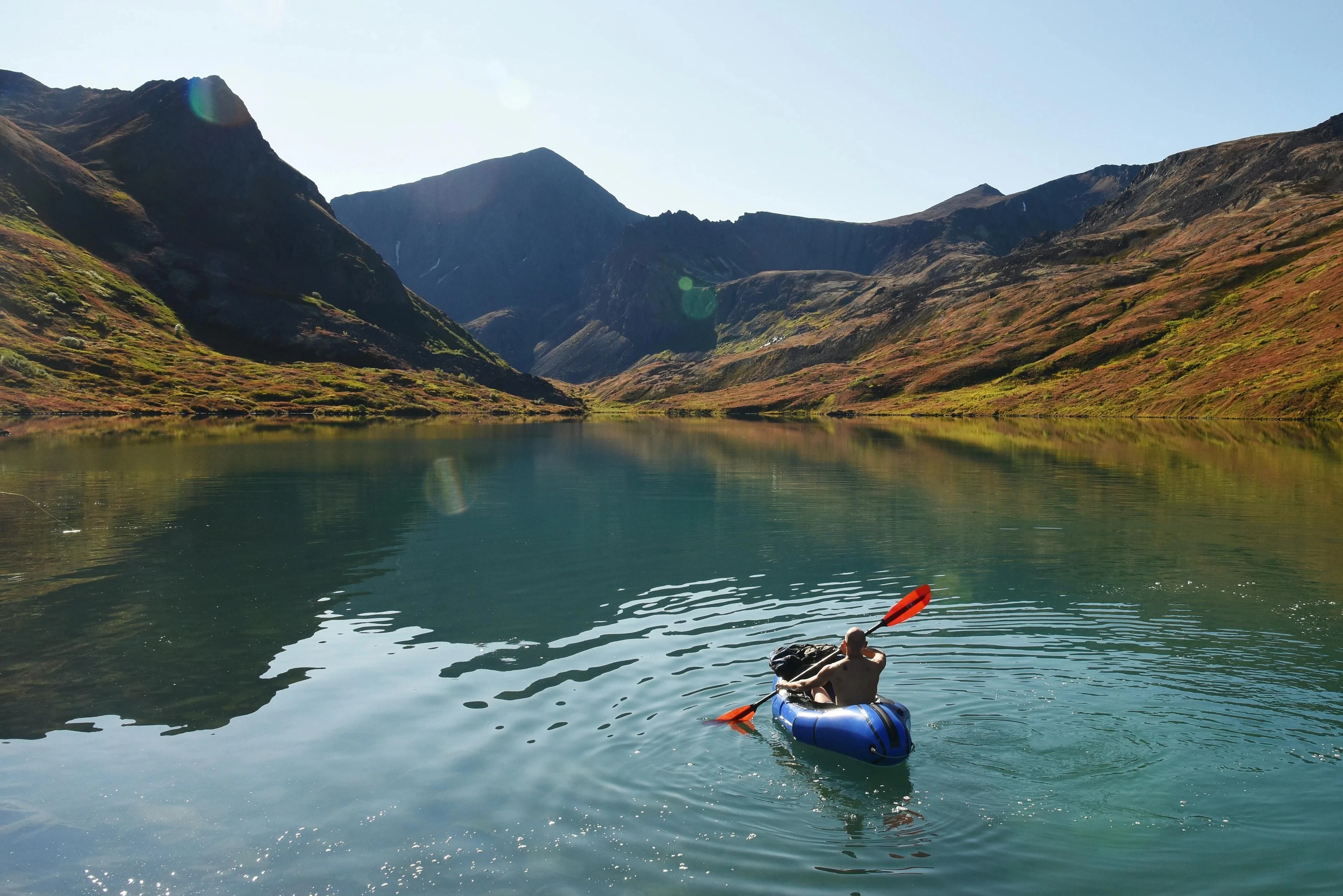 A paddler crosses a mountain lake in a loaded packraft.