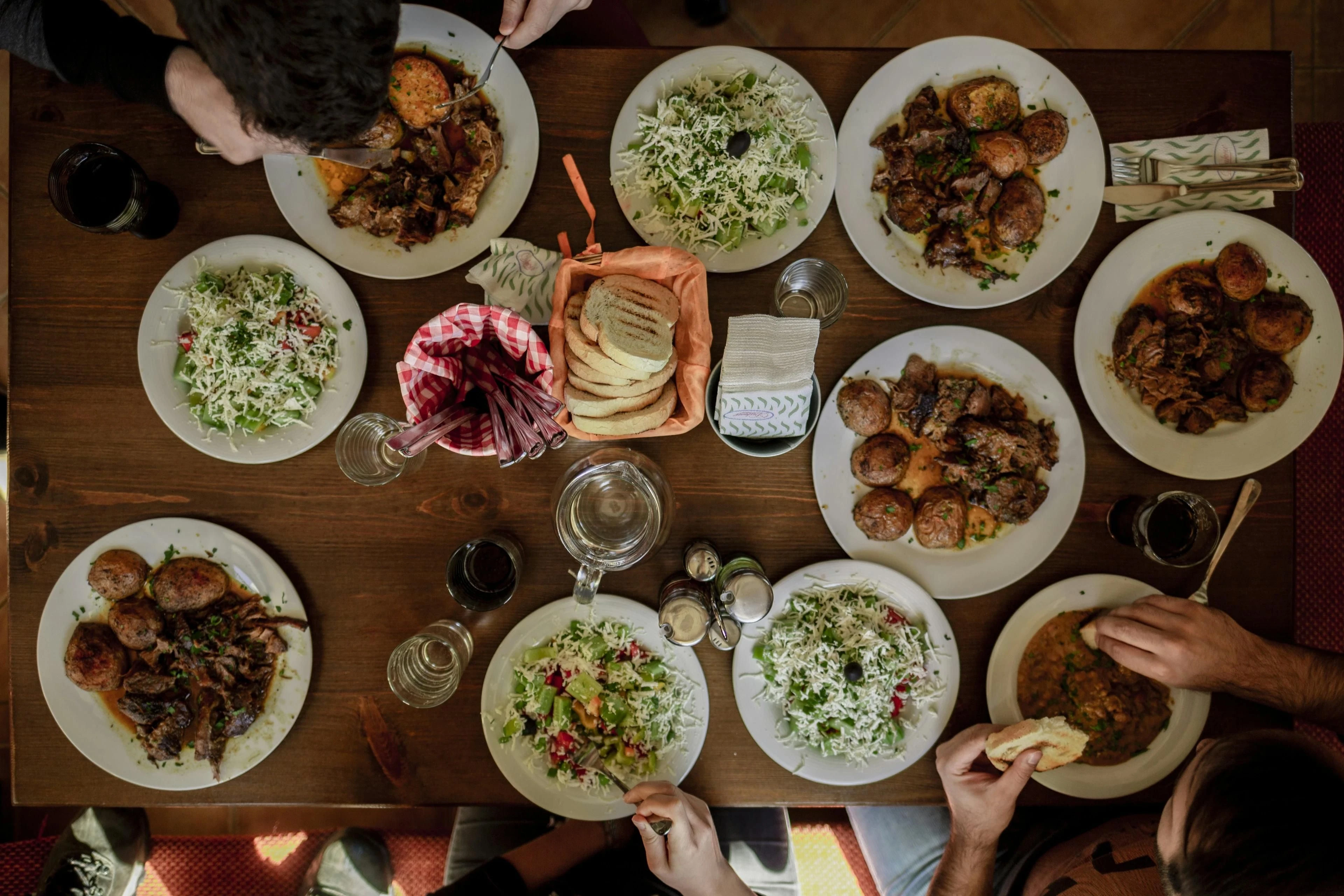 People share bread, salads and hot dishes around a wooden table in a mountain hut.