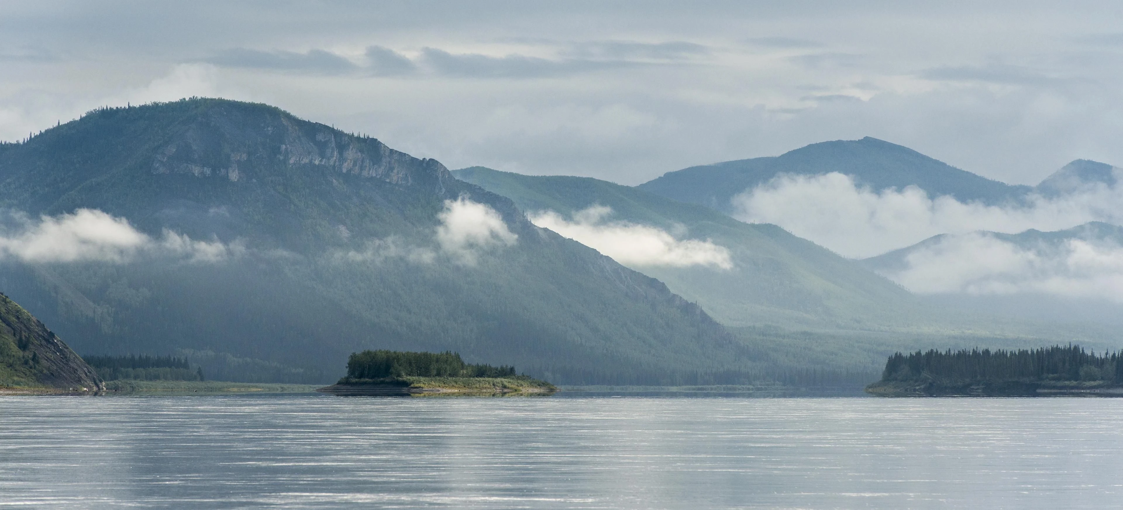 A broad river beneath low cloud and forested mountain slopes.