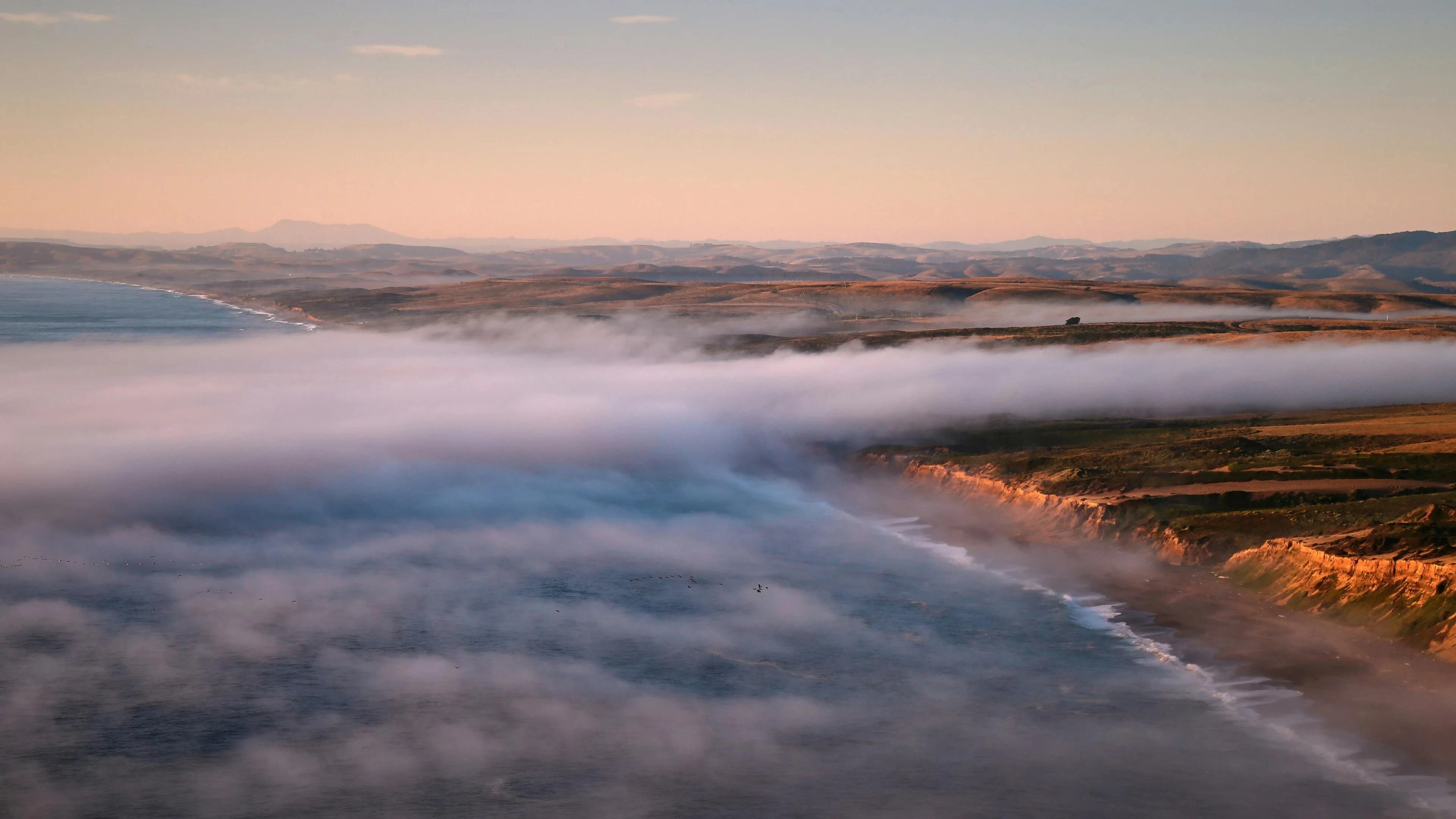 Coastal fog drifts over cliffs and the shoreline.