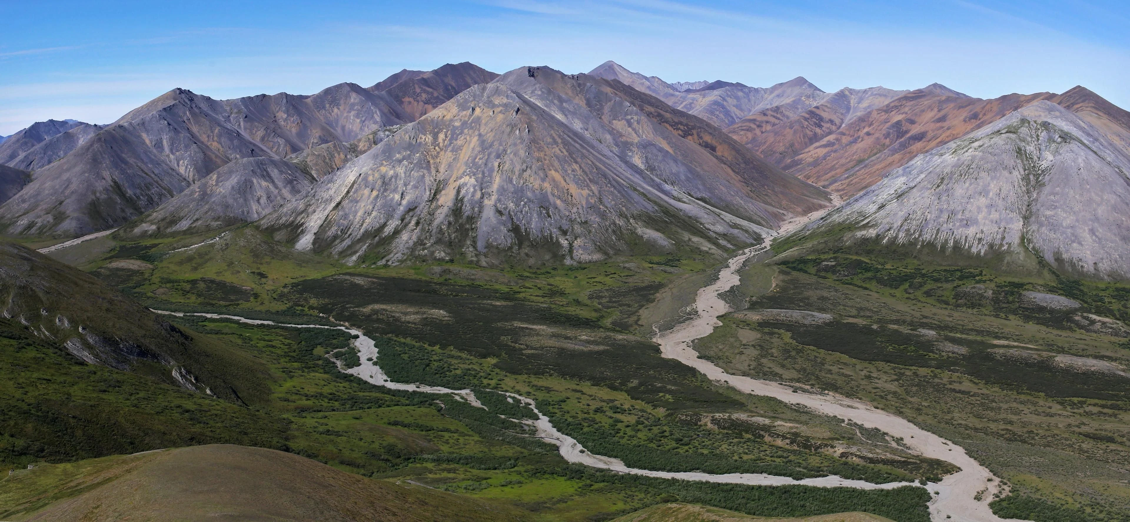 Pale streams wind between green valley floors and steep, bare mountain ridges.