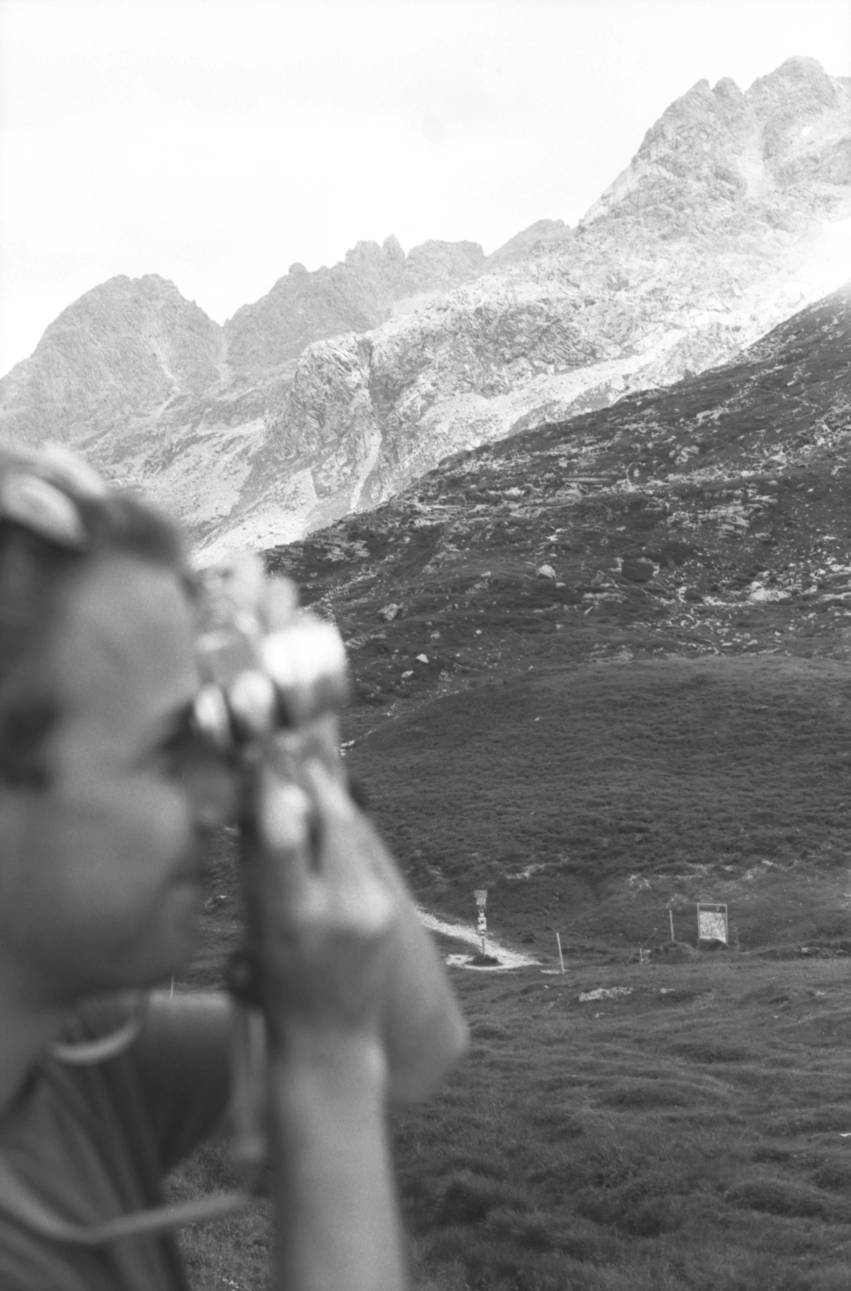Hands hold a film camera while photographing a mountain landscape.