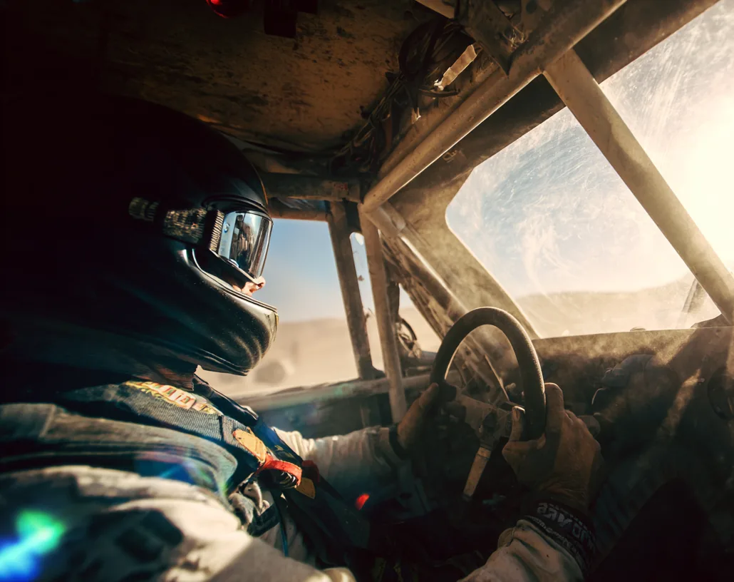 A driver wearing a full-face helmet and gloves at the controls of a race cockpit.