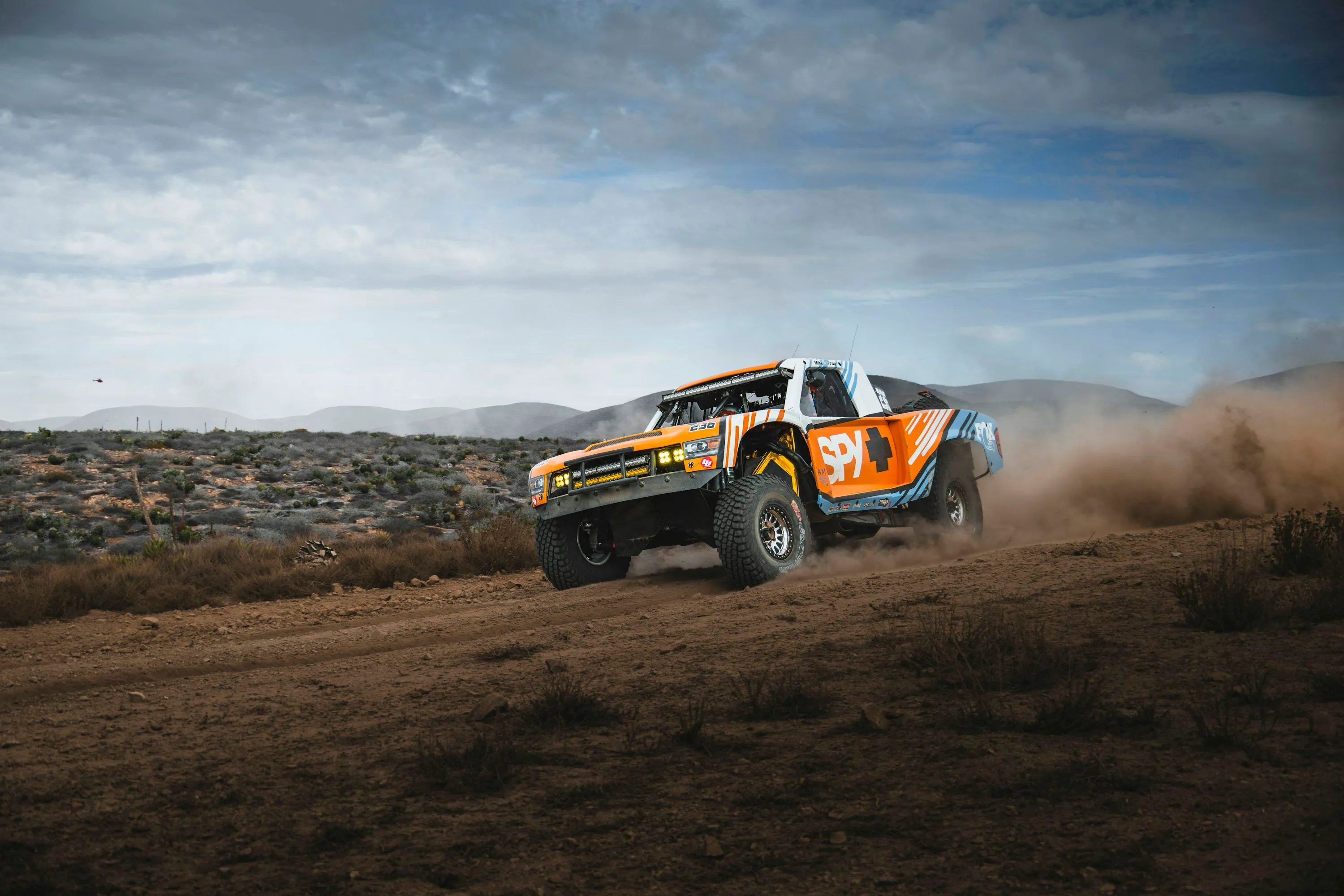 A race truck works its suspension through rough desert ground.