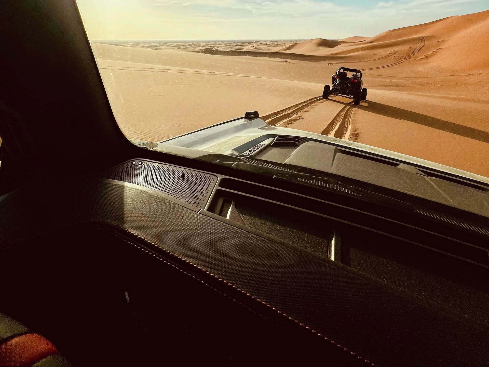 View from a Ford Bronco Raptor across tyre tracks and sand dunes.